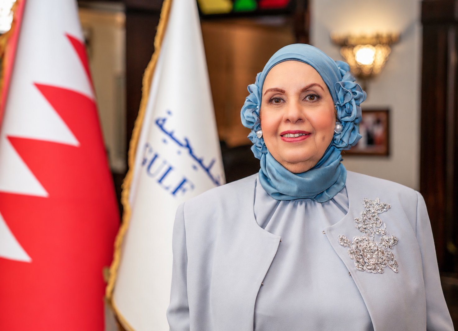 Portrait of Prof. Dr. Mona bint Rashid Al-Zayani in front of the Bahrain and Gulf University flags